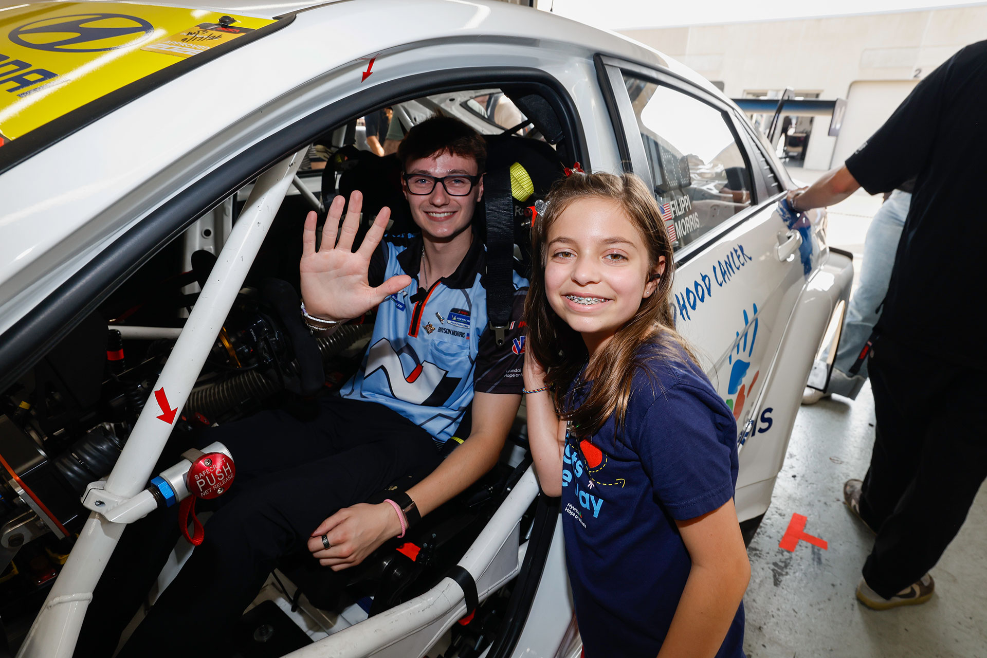 Hyundai Hope on Wheels National Youth Ambassador waving beside a Hyundai race car